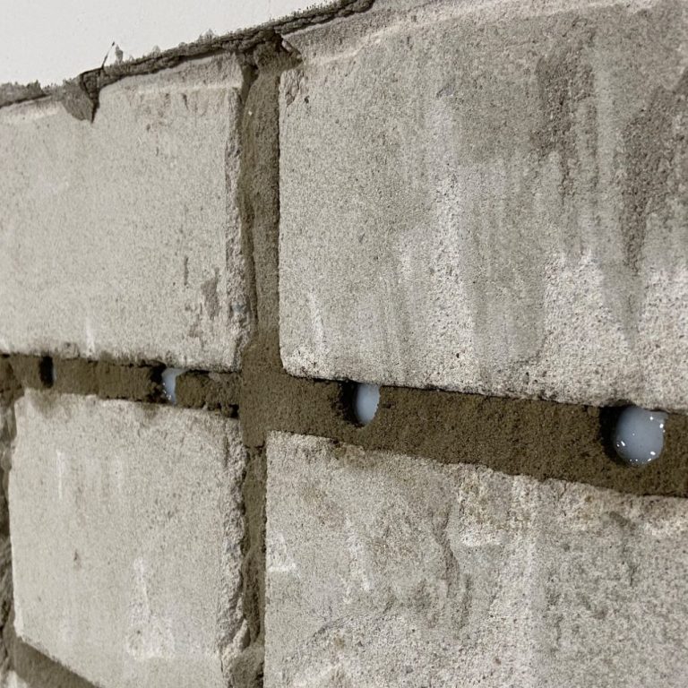 Nahaufnahme einer Mauer aus Kalksand-Stein mit einer Creme verfüllten Bohrreihe.