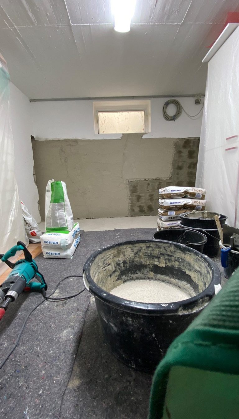 Ein Handwerker trägt schwarzen Mörtel mit einer Kelle auf eine graue Fläche auf.