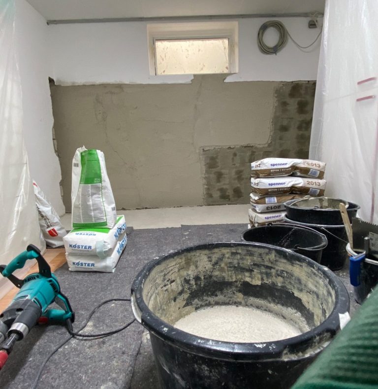 Ein Handwerker trägt schwarzen Mörtel mit einer Kelle auf eine graue Fläche auf.