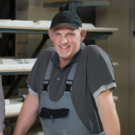 Mann in Arbeitskleidung mit einem Lächeln, steht in einer Werkstatt.