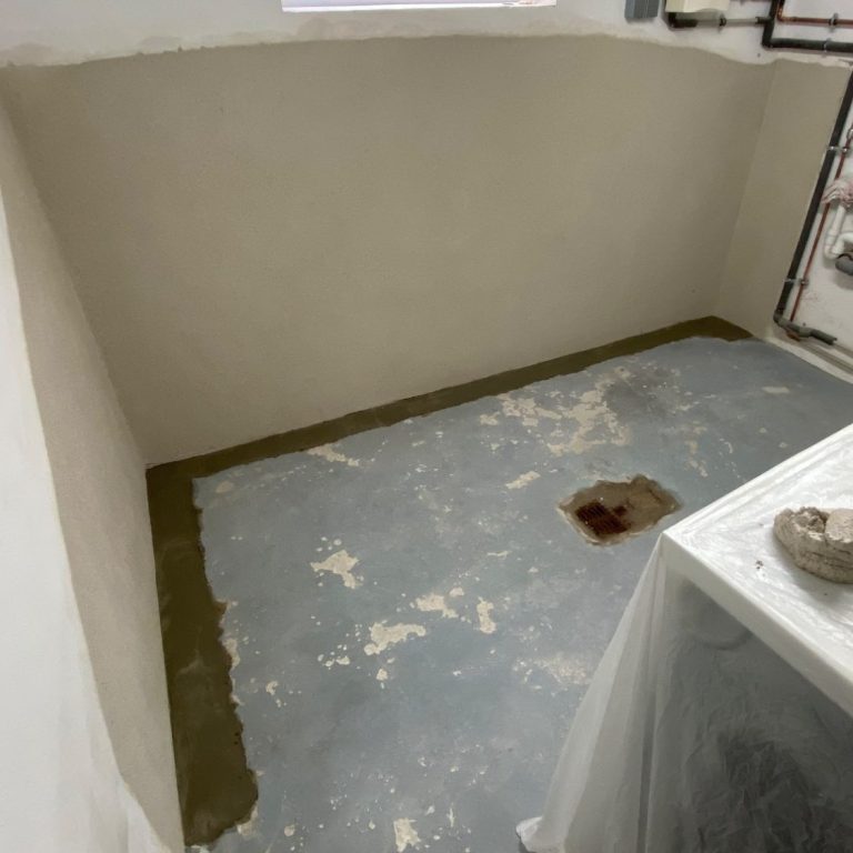 Leere Innen-Kellerraum mit grauem Boden und teilweise sanierten Wänden.