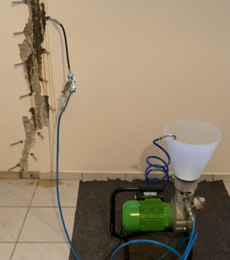 Eine Wand mit Rissen und einer Hochdruck-Injektionsmaschine zur Riss-Reparatur auf einem grauen Teppich.
