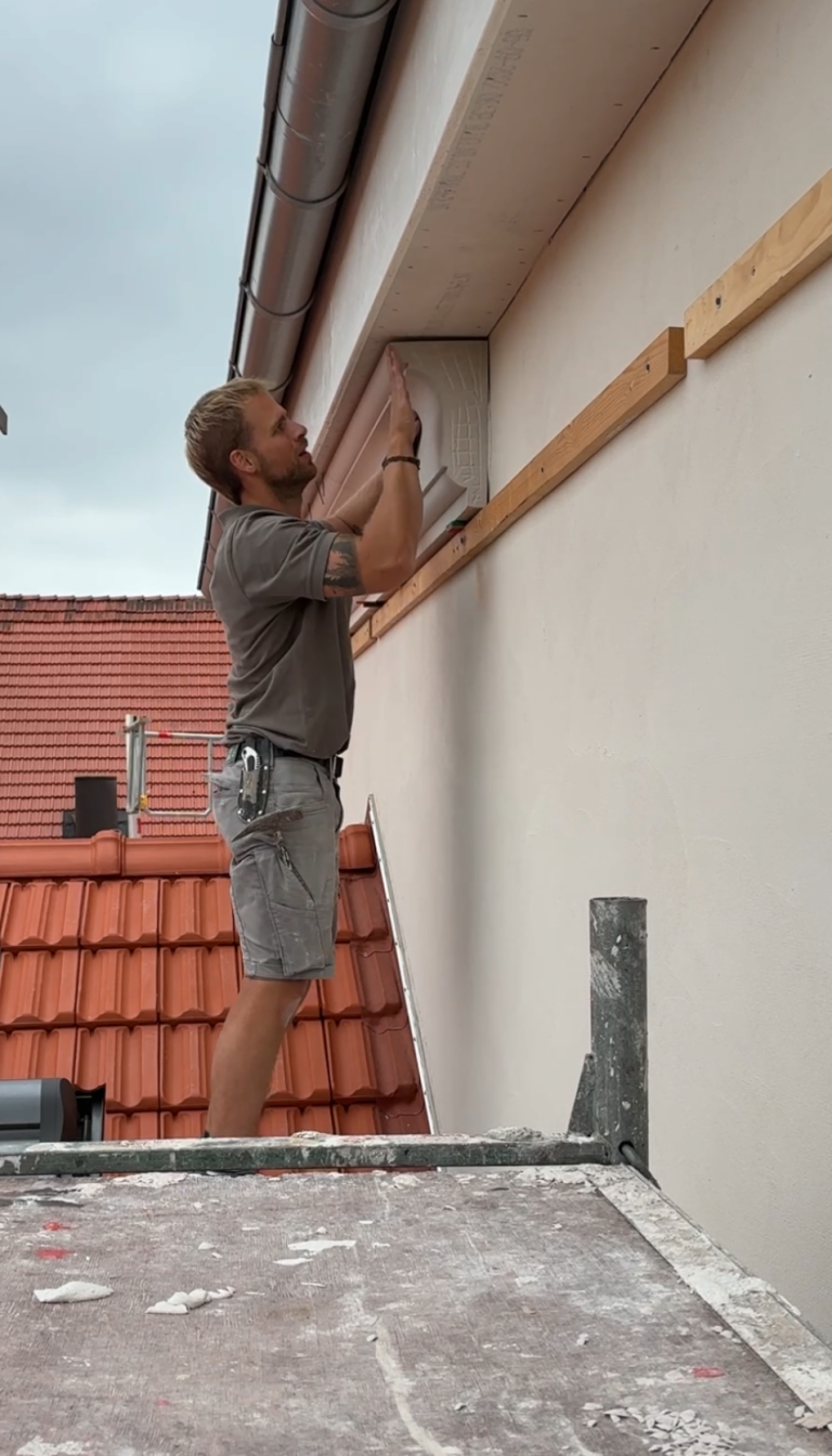 Fenster mit Bogen und dekorativen Elementen an einer hellen Hausfassade.