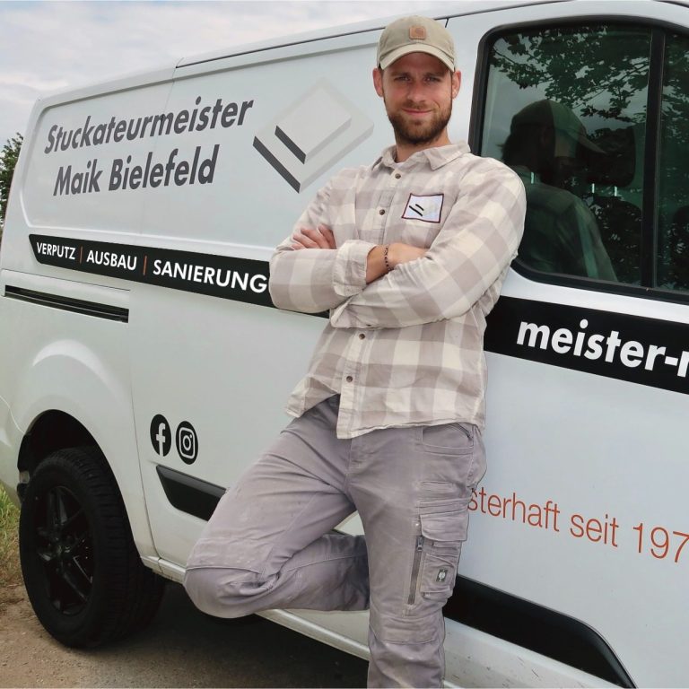 Stuckateurmeister Maik Bielefeld Mann im grauen Arbeitsanzug steht neben einem weißen Transporter mit Firmenlogo.